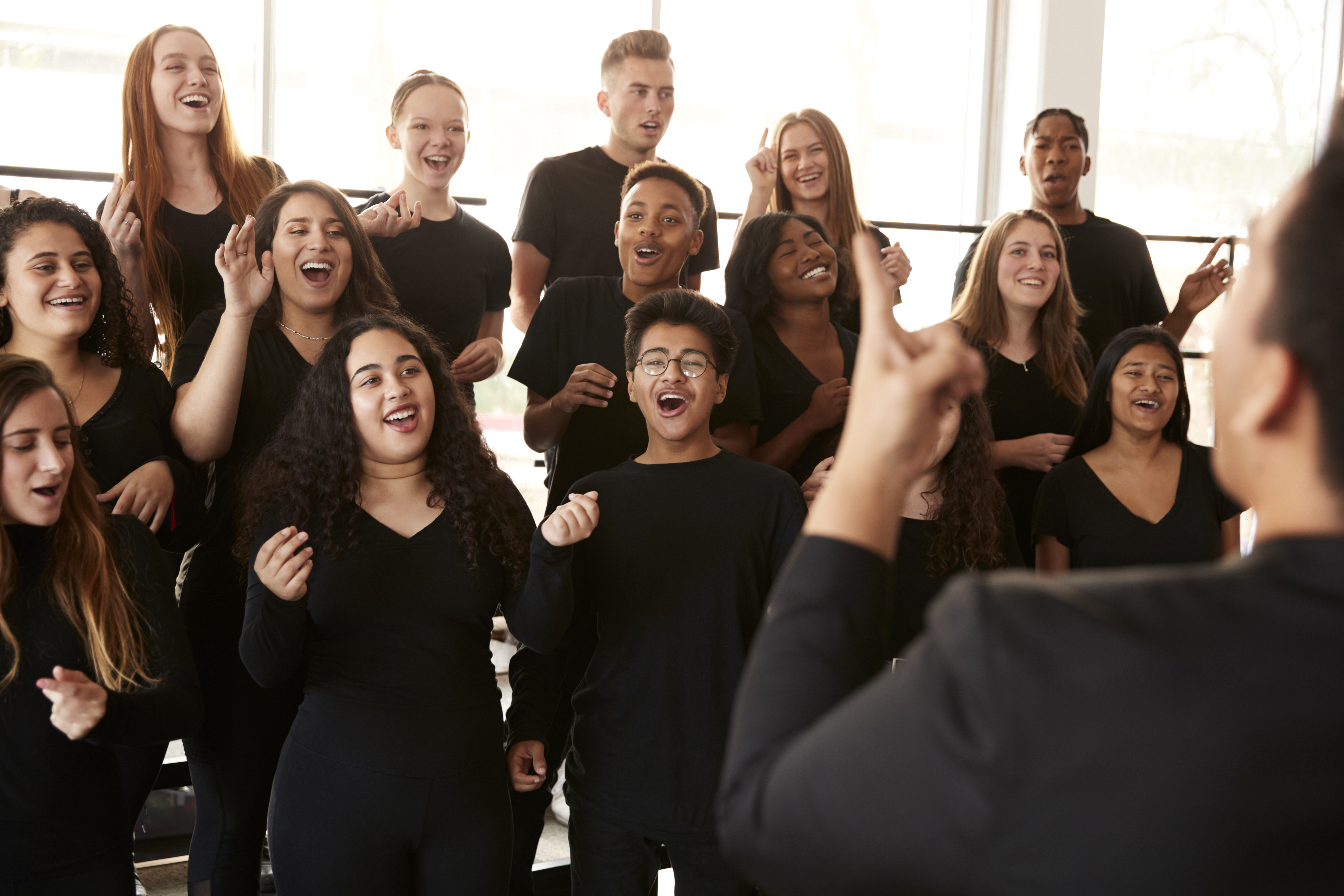 Male And Female Students Singing In Choir With Teacher At Performing Arts School